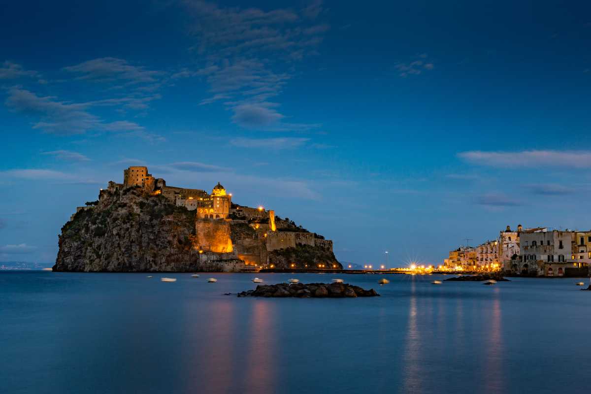 Vista panoramica su una spiaggia di Ischia con mare cristallino, sabbia dorata e vegetazione mediterranea